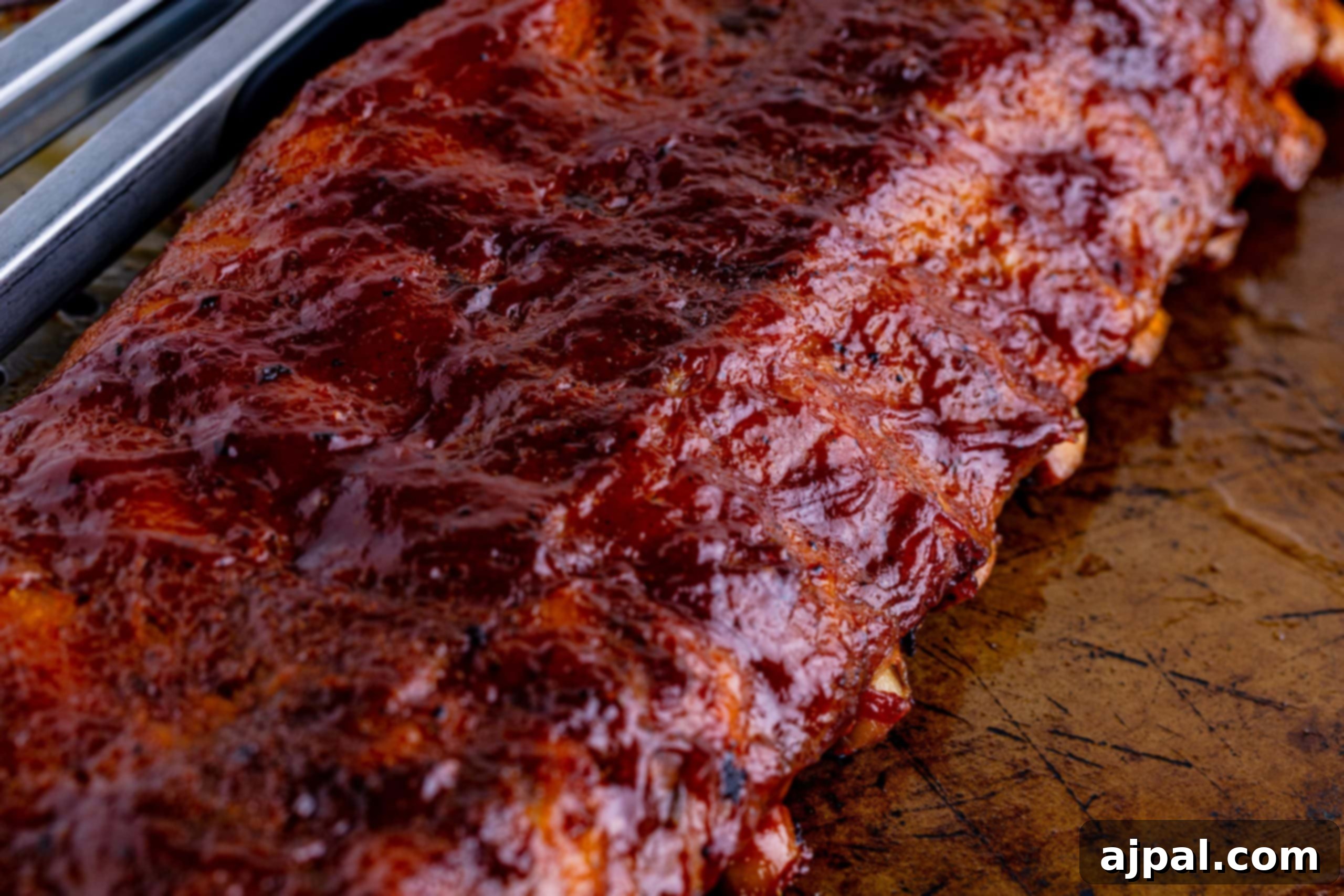 Perfectly Tender Oven Baked Ribs 9 Delicious oven-baked ribs, generously slathered in barbecue sauce, resting on a baking sheet.