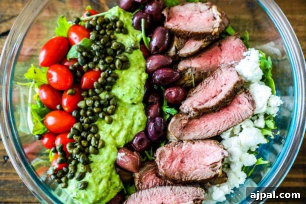 An overhead view of the creamy avocado steak salad, showcasing the beautifully arranged components of tender steak, vibrant tomatoes, capers, olives, and crisp lettuce, all coated in the verdant dressing.