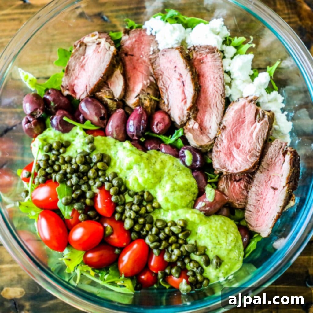 A vibrant creamy avocado steak salad artfully arranged in a glass bowl, showcasing tender steak, bright cherry tomatoes, and tangy capers with a lush green dressing.