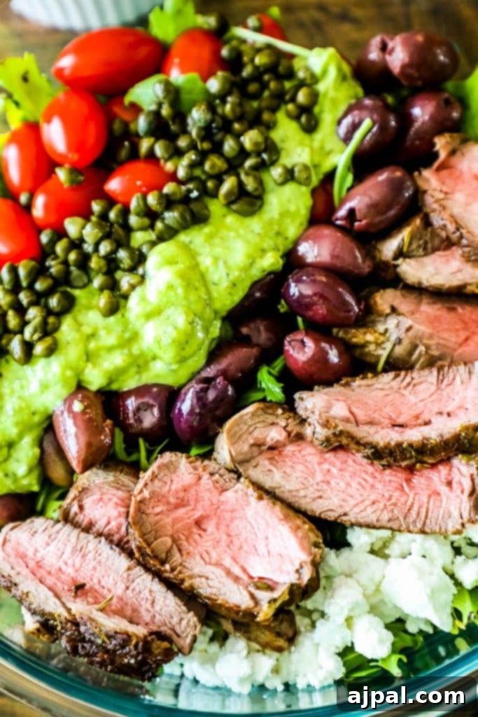 A delicious bowl of creamy avocado steak salad, featuring ripe tomatoes and briny capers, glistening with the rich green dressing.