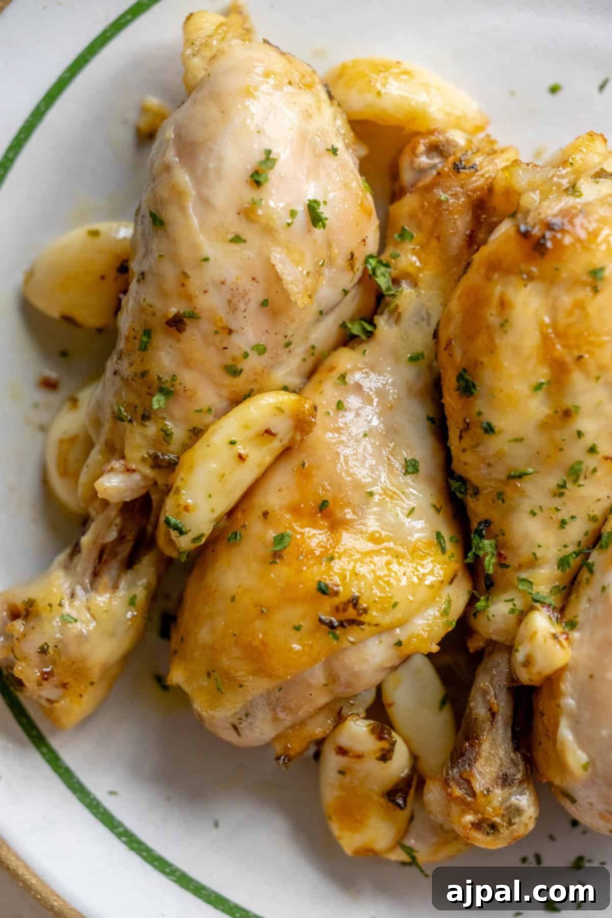 Zesty Greek Chicken Drumsticks 2 Close-up of Greek chicken drumsticks with roasted garlic cloves and herbs on a white dish.