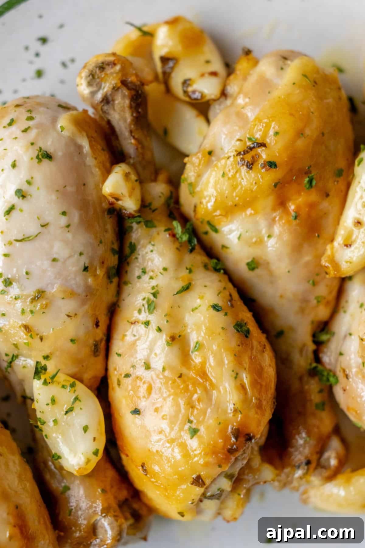 Zesty Greek Chicken Drumsticks 3 Close-up of Greek chicken drumsticks, roasted to perfection and garnished with chopped herbs and garlic cloves on a white plate.