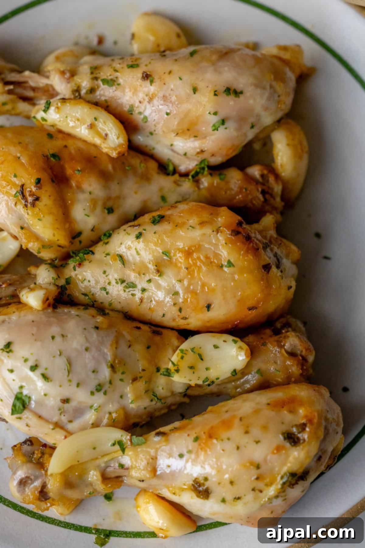 Zesty Greek Chicken Drumsticks 4 Greek chicken drumsticks, cooked to perfection, are garnished with chopped herbs and fragrant garlic cloves on a plate.