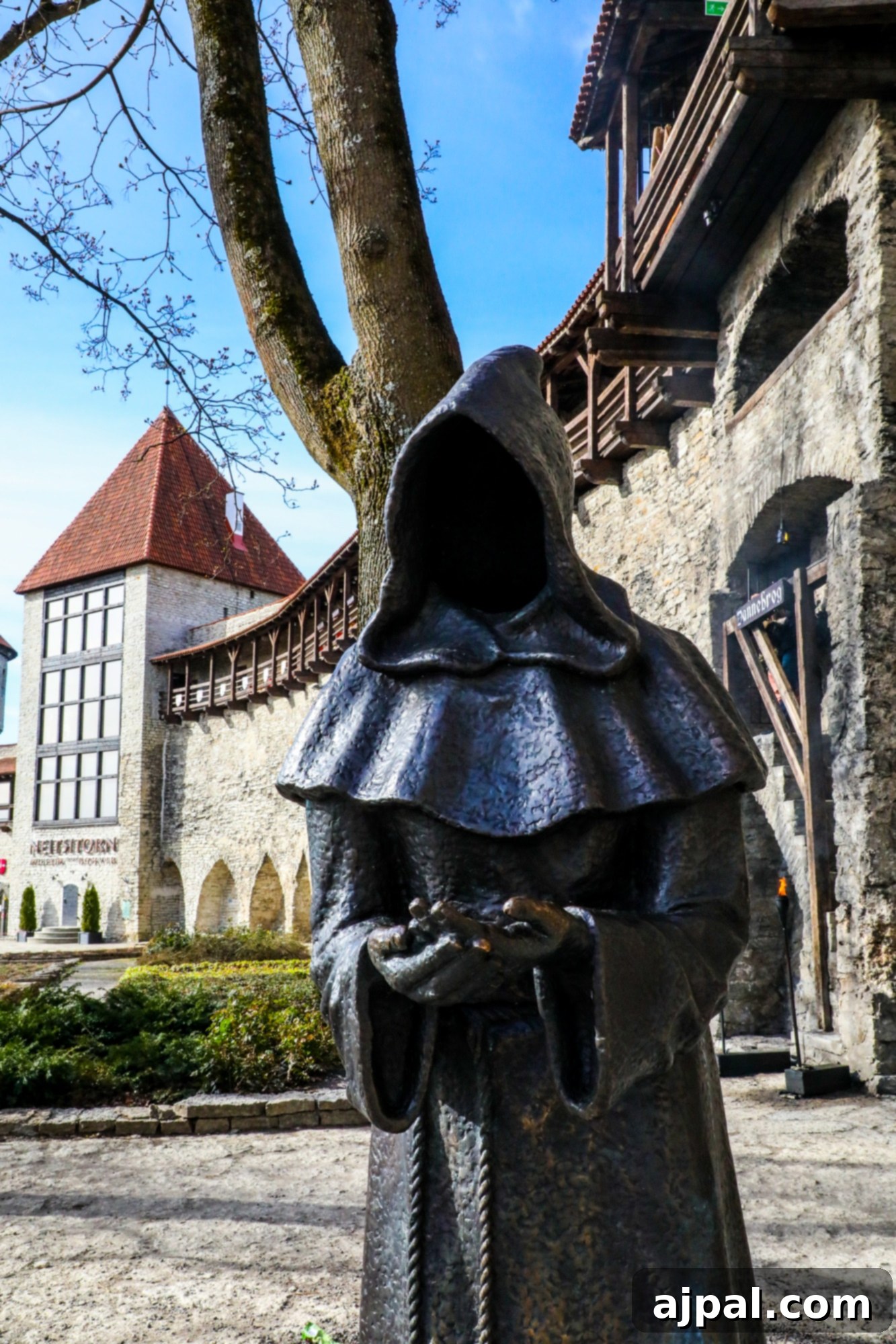 A weathered monk statue standing outside a medieval tower wall in Tallinn, Estonia, adding to the ancient ambiance.