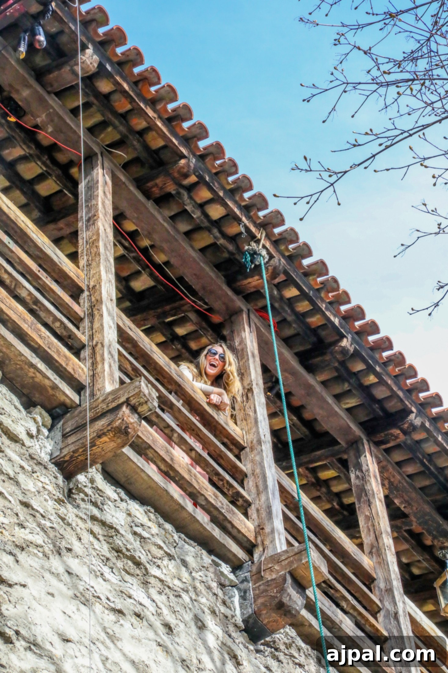A woman standing on a wooden balcony of a tower cafe, overlooking Tallinn, Estonia's picturesque Old Town, enjoying the view with a friend.
