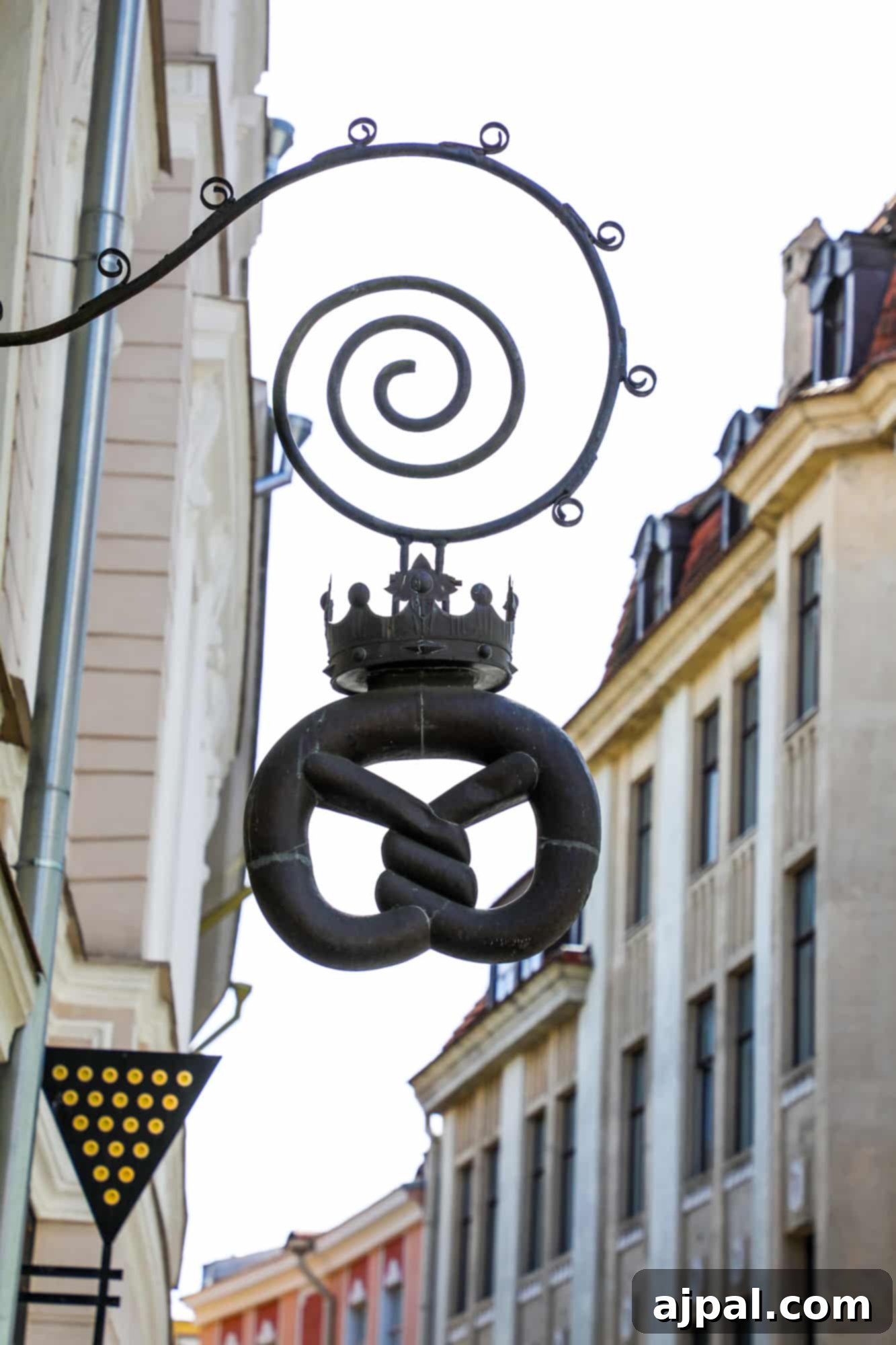 A quaint metal pretzel sign hanging outside Loiri Nunne Bakery Pastry Shop in Tallinn, Estonia, inviting passersby to enjoy its delights.