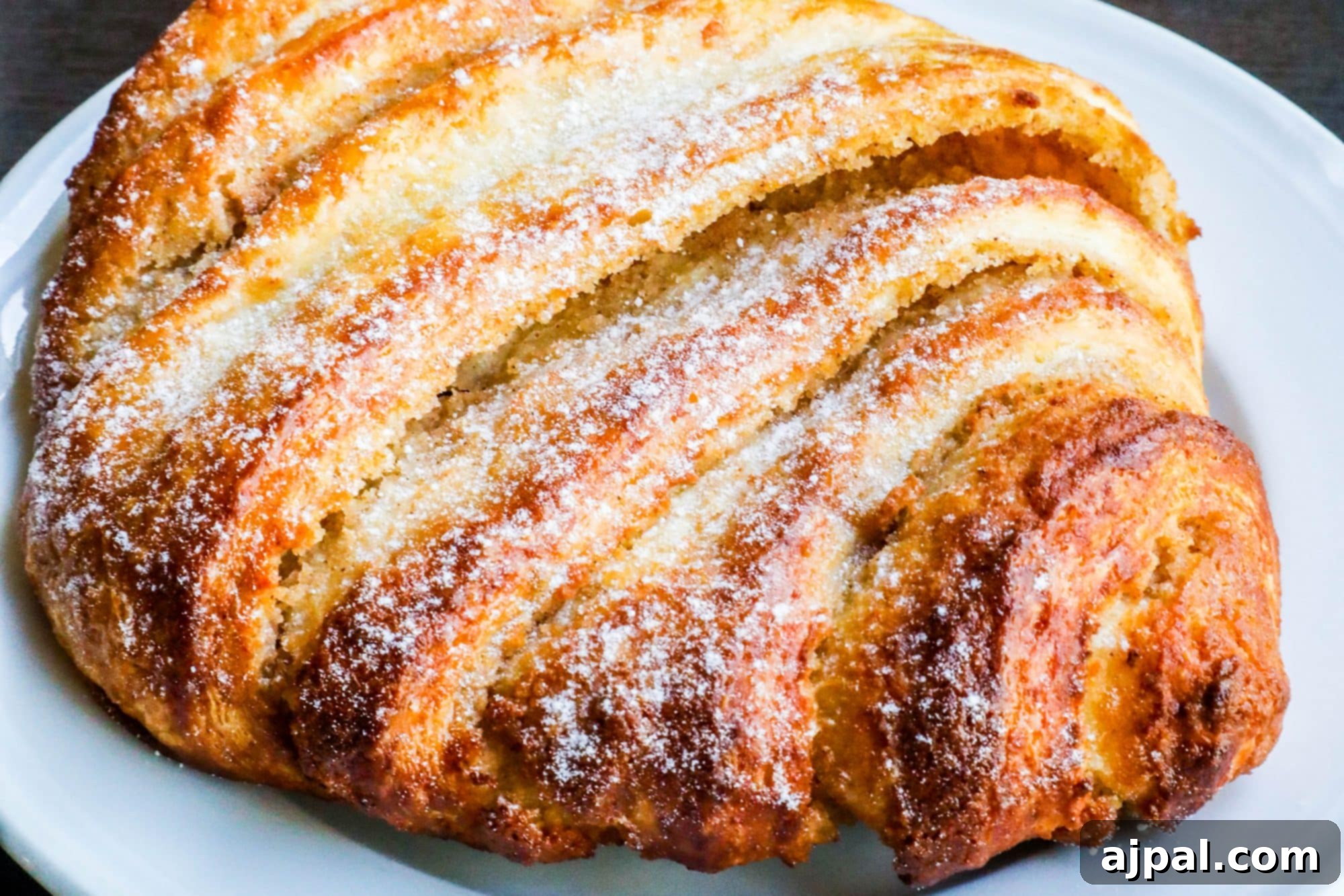 A delectable Estonian Kringle, a braided cinnamon pastry dusted with powdered sugar, served on a white plate.