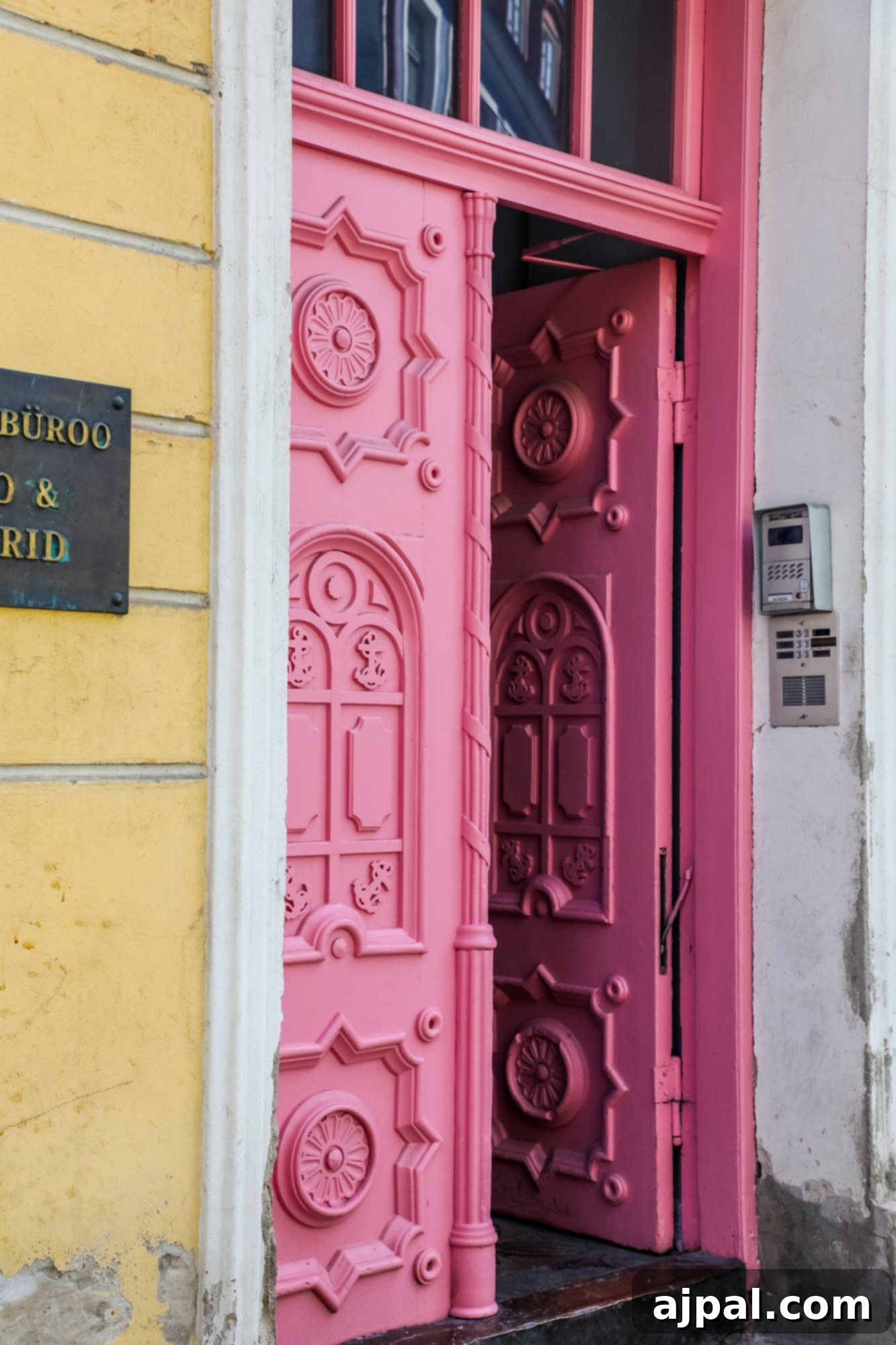 A beautifully ornate pink decorative door on a yellow building in Tallinn, Estonia, highlighting the city's vibrant and artistic details.