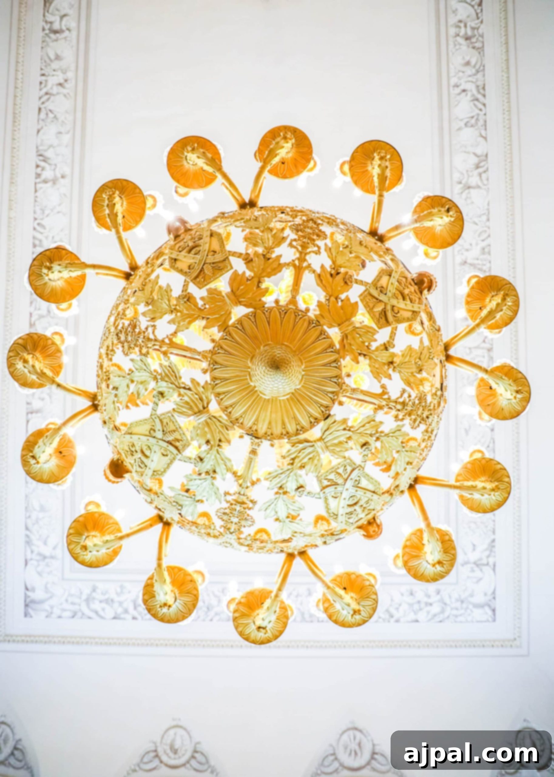 An ornate gold chandelier descends from the ceiling of a grand room in Saint Petersburg, Russia, possibly at Yusupov Palace.