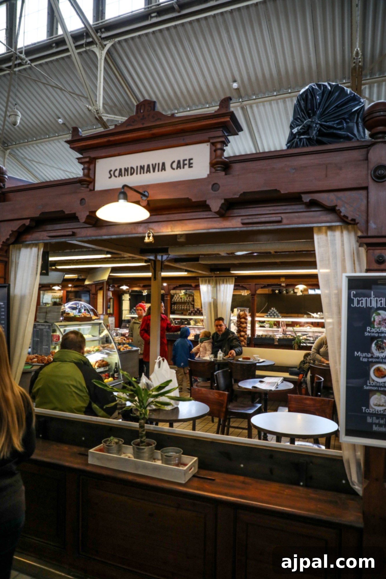 A woman enjoys a meal at one of the cozy market stalls in Helsinki's Old Market Hall, bustling with local life.