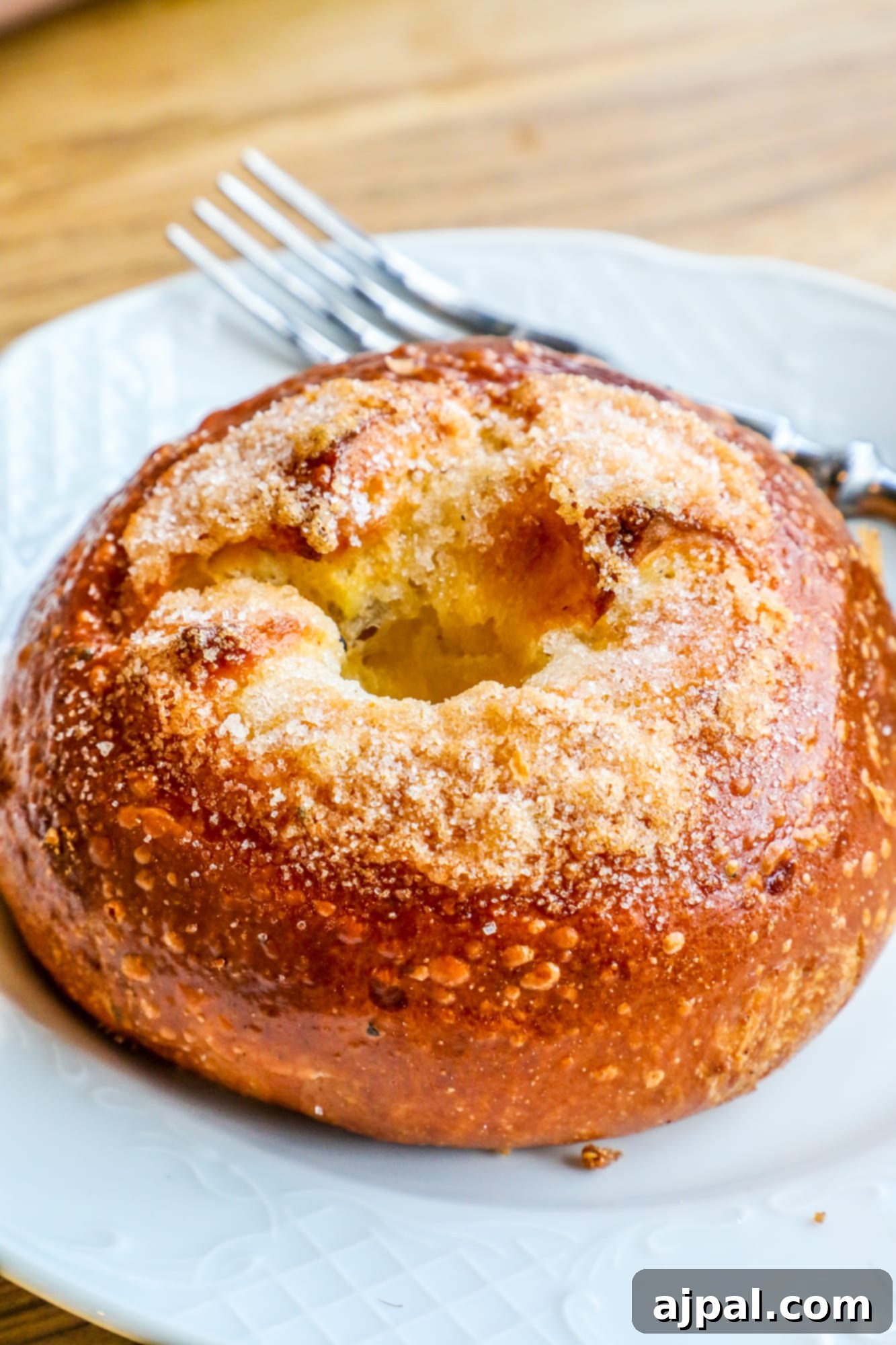 A perfectly glazed cinnamon apple bun sits invitingly on a white plate in Helsinki, ready to be enjoyed.