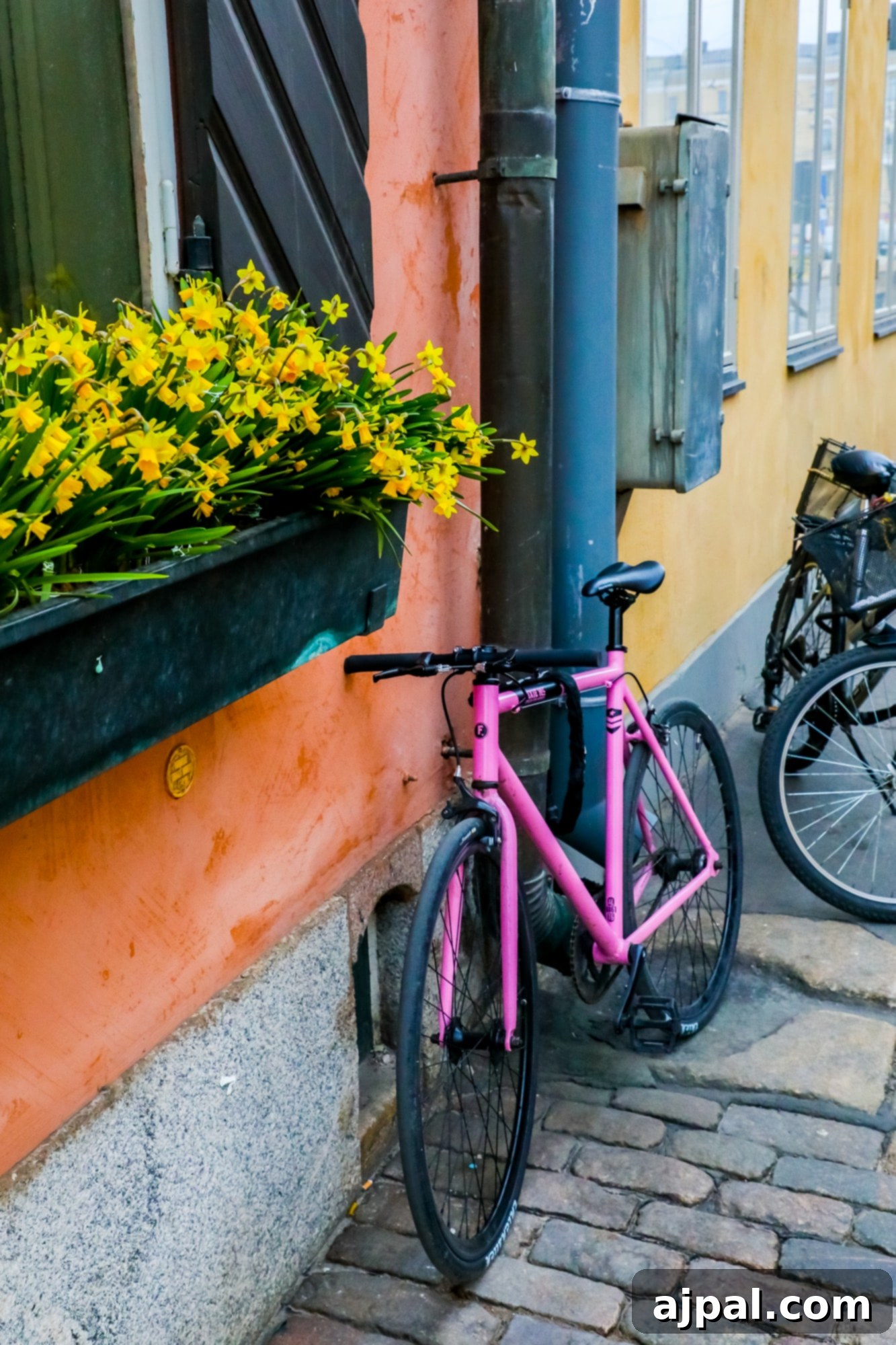 A stylish pink bicycle leans against a textured brick wall in Helsinki, adding a pop of color to the urban landscape.