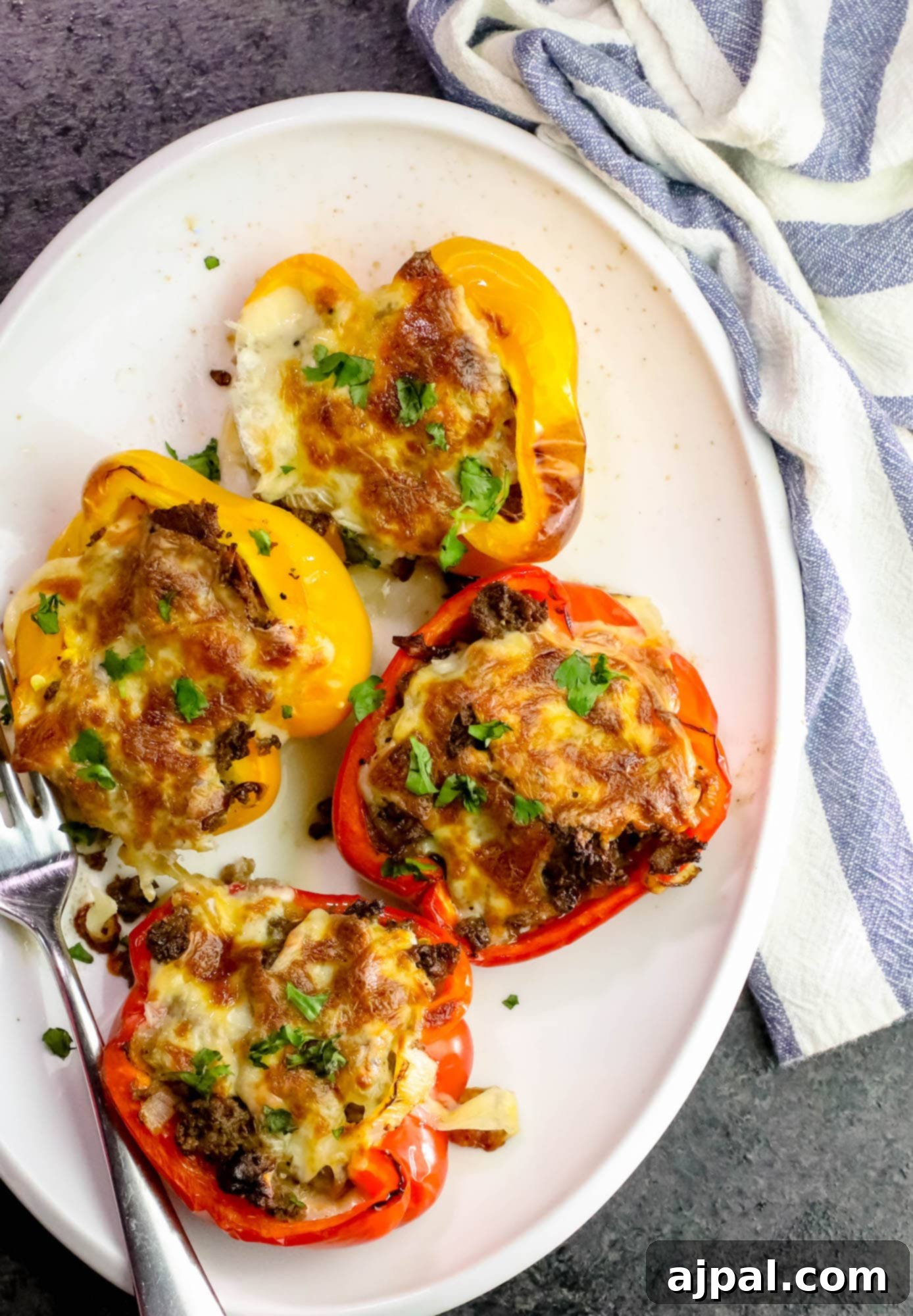 Loaded Cheesesteak Stuffed Peppers 2 A plate featuring two vibrant bell peppers generously filled with melted provolone cheese and savory Philly cheesesteak mixture.