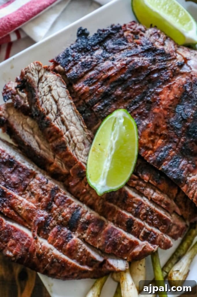 Grilled flank steak slices arranged on a white plate, garnished with fresh lime wedges, ready to be served.