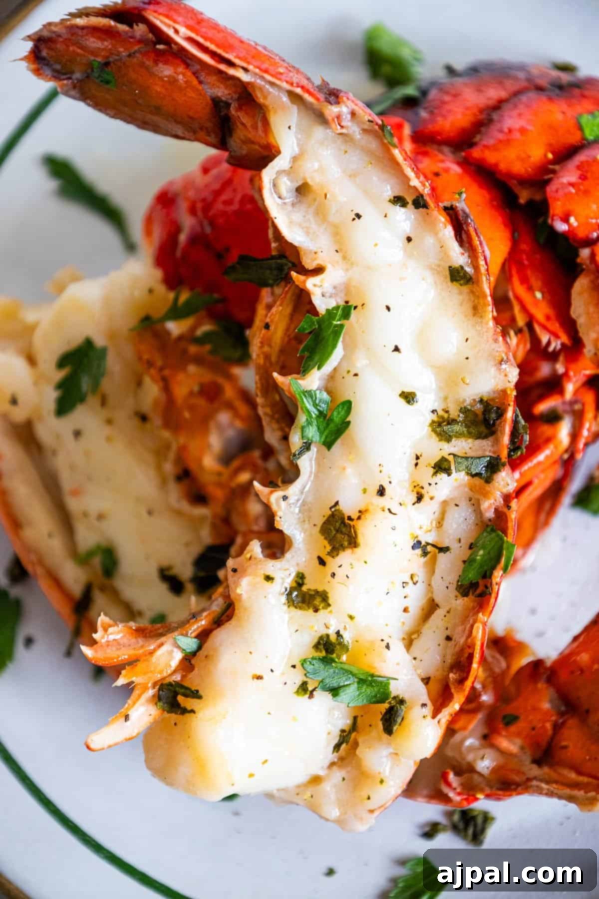 Decadent Butter Poached Lobster Tails 2 Close-up of butter-poached lobster tails in a garlic lemon cream sauce, garnished with fresh herbs and lemon slices.