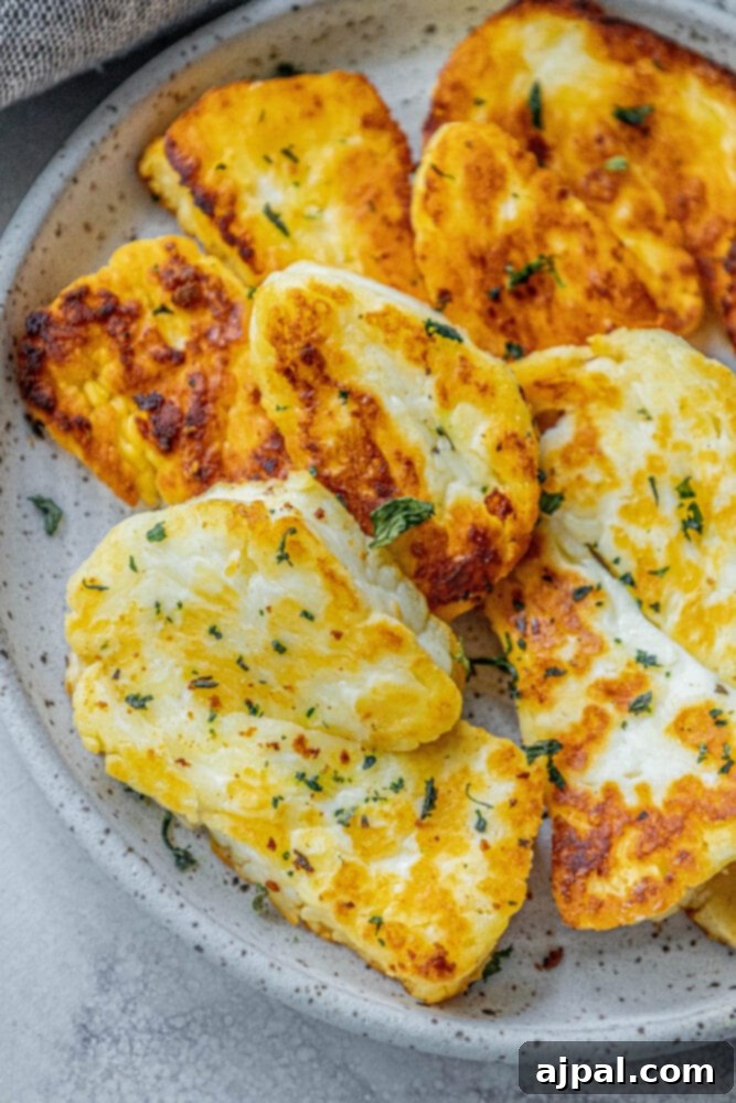 Greek Pan Fried Halloumi Recipe 2 Crispy, golden-brown slices of pan-fried halloumi cheese garnished with dried mint on a white plate, ready to be served as an appetizer.