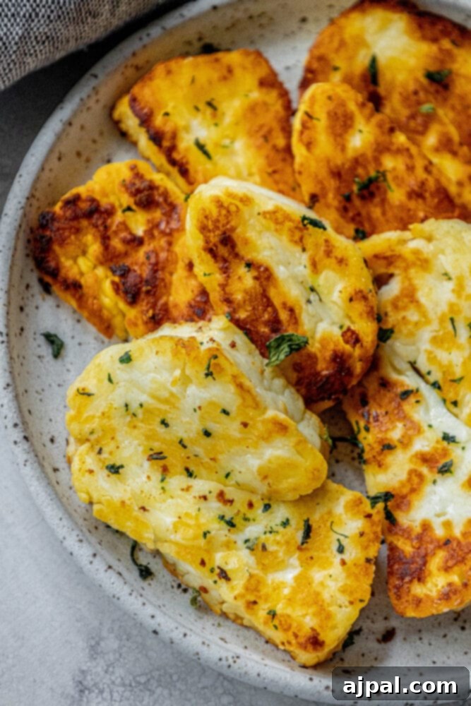 Greek Pan Fried Halloumi Recipe 11 A close-up picture of browned slices of halloumi cheese on a white plate with dried mint on top, highlighting the crispy texture and delicious appeal of the dish.