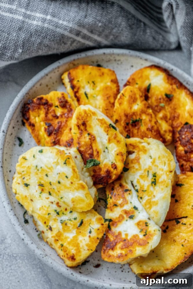 Greek Pan Fried Halloumi Recipe 3 Golden-brown slices of halloumi cheese, fried to perfection, presented on a white plate with a sprinkle of dried mint, capturing its crispy texture and delicious appeal.