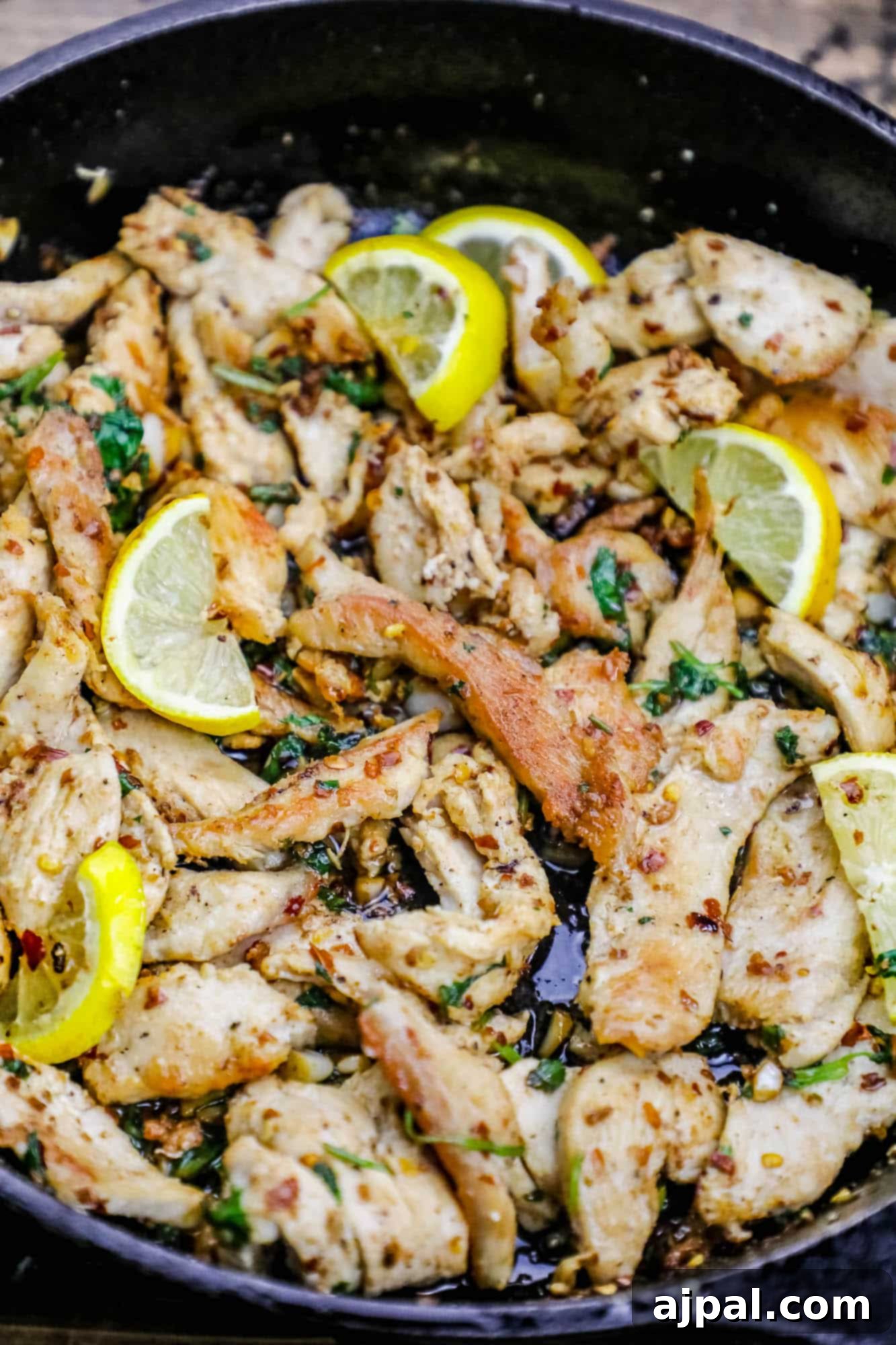 Crispy pan-fried chicken strips generously coated with red pepper flakes, fresh garlic, and bright lemon wedges, served in a skillet.
