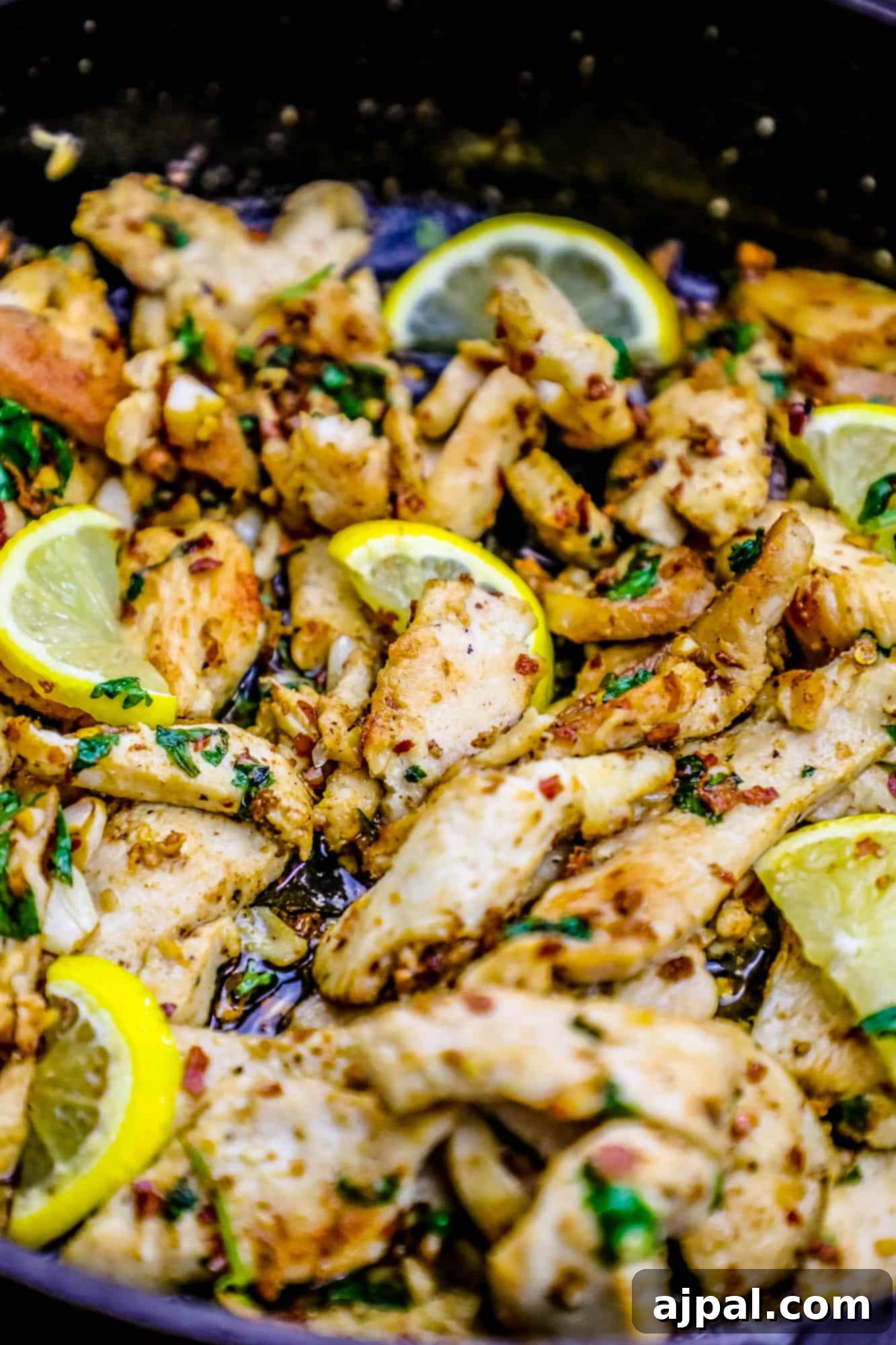 Pan-fried low-carb chicken strips with lemon slices and fresh herbs, artfully arranged in a skillet.