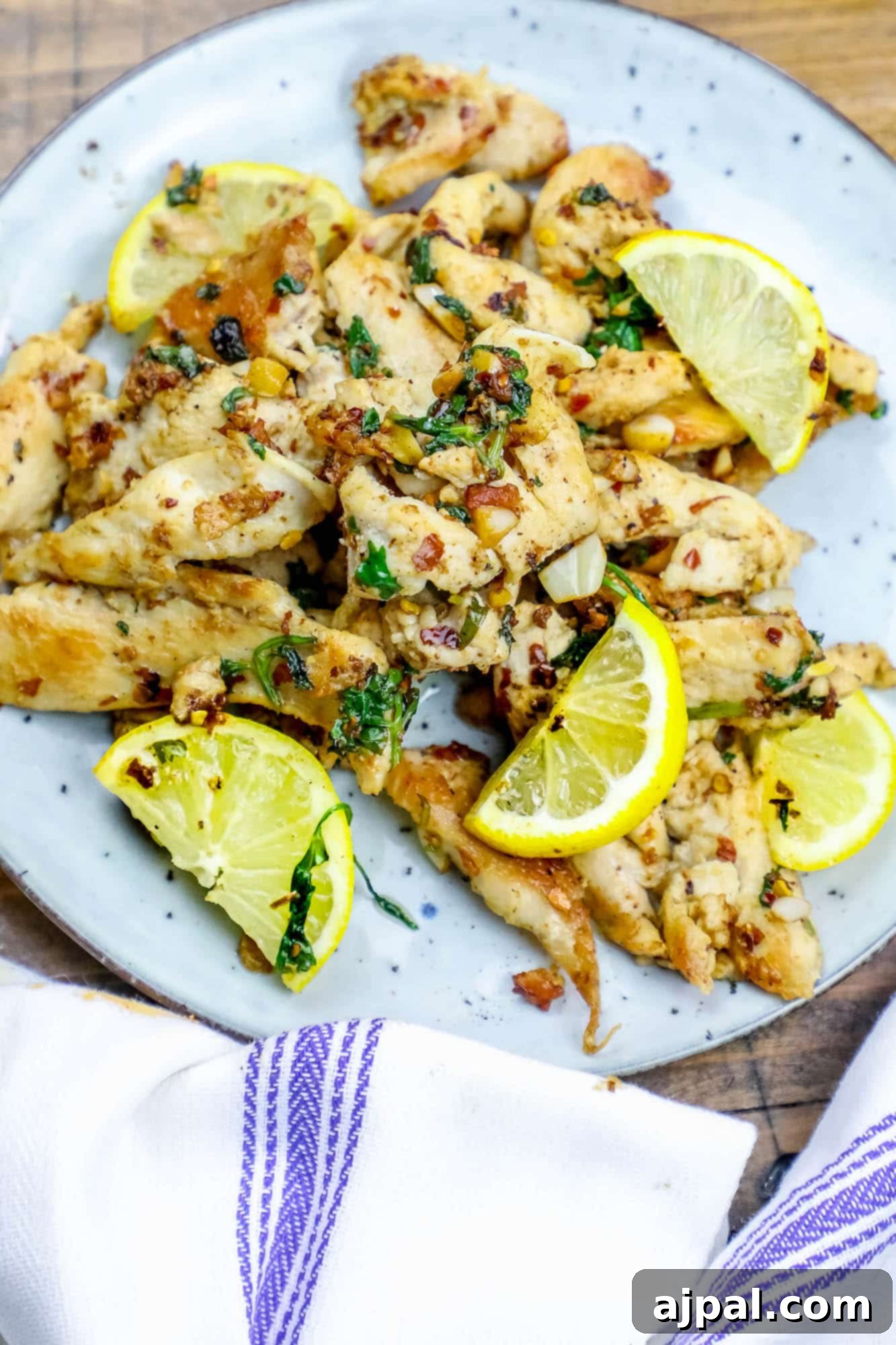 Golden pan-fried chicken strips bathed in lemon garlic butter, garnished with fresh herbs, served on a white plate.