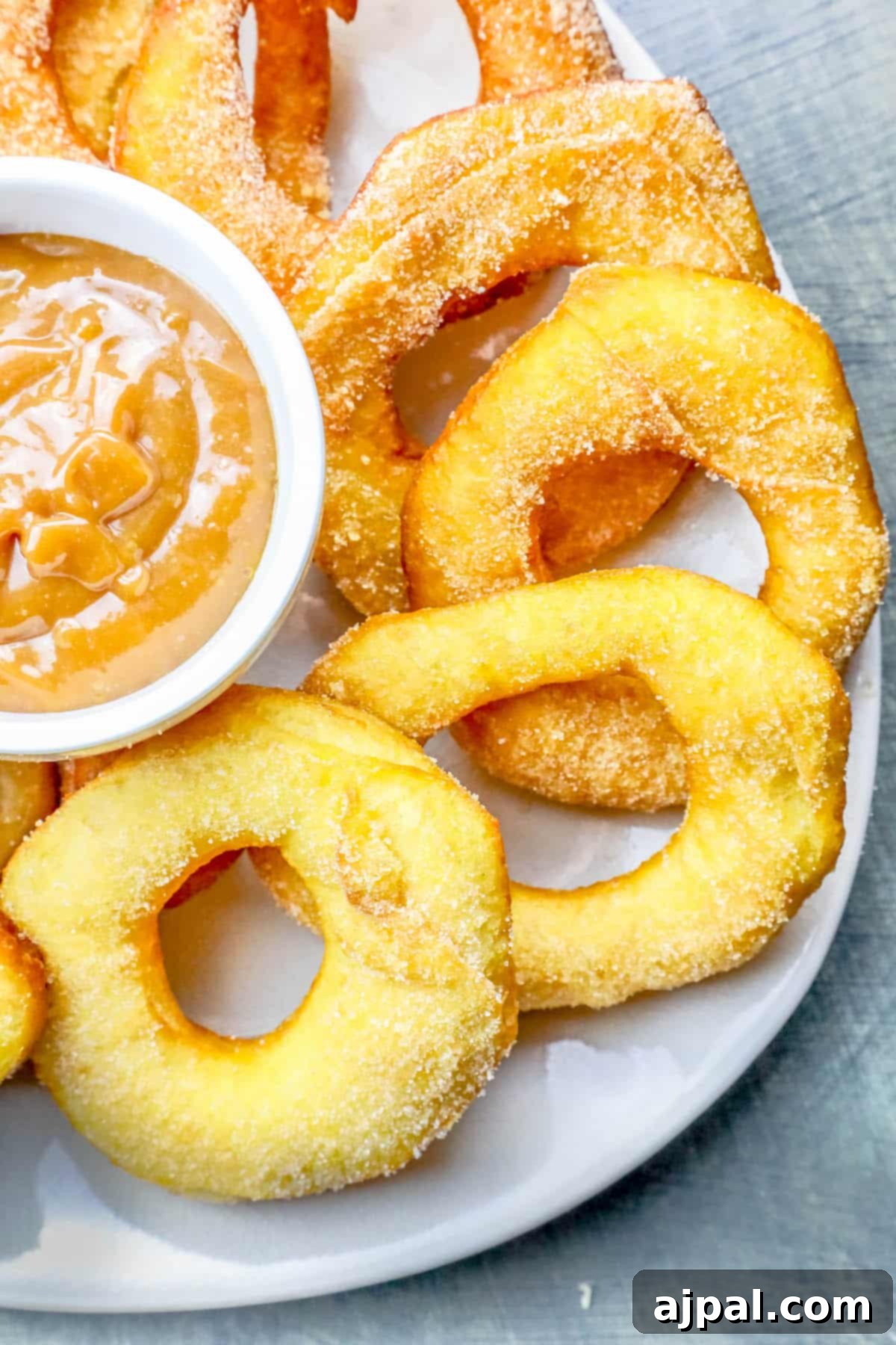An inviting overhead shot of warm mulling spiced donuts and donut holes, beautifully coated in a sugary spice blend, presented on a plate next to a small bowl of dipping sauce.