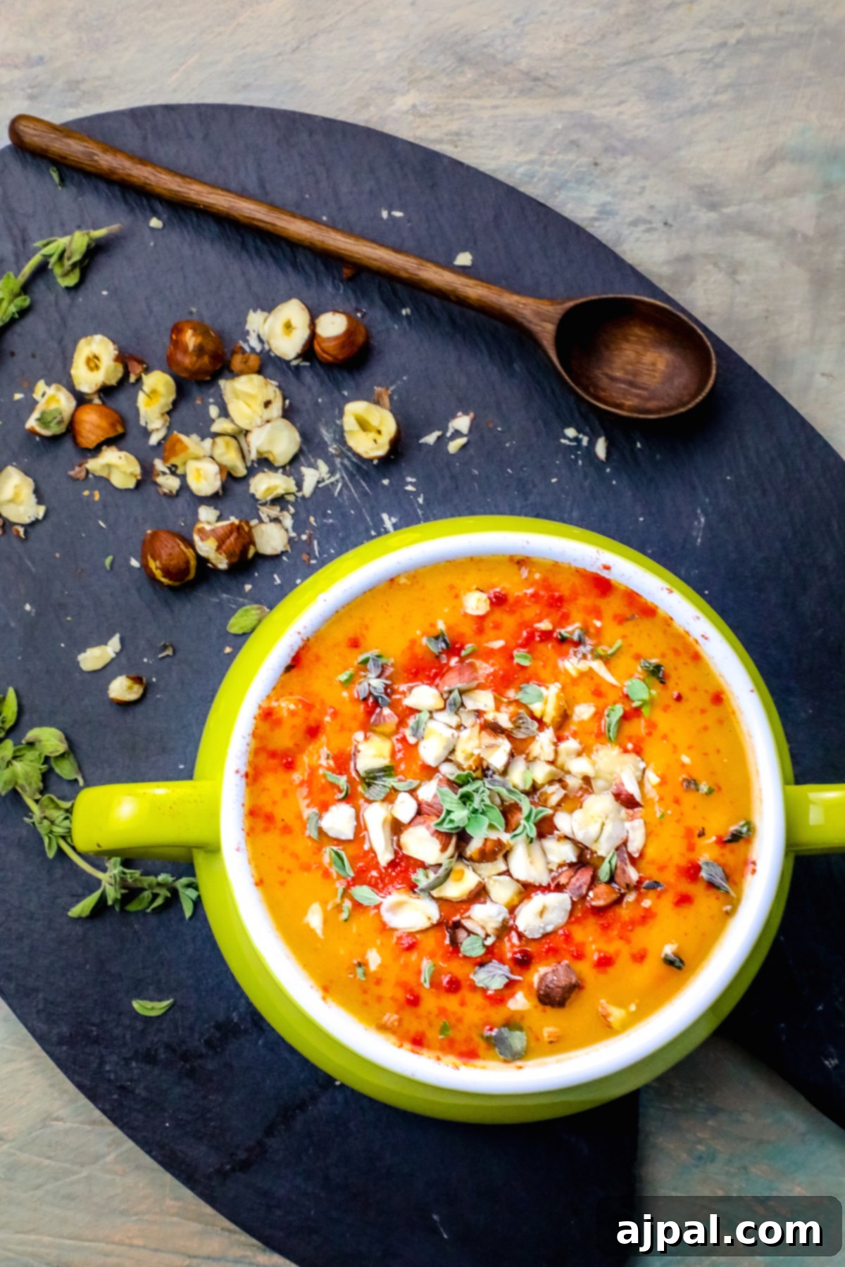 Velvety Sweet Potato Soup with Toasted Hazelnuts 2 A vibrant orange bowl of creamy sweet potato soup garnished with toasted hazelnuts and a sprig of fresh herb.