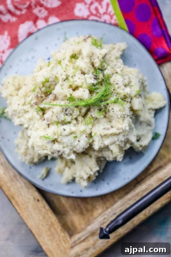 A large bowl of creamy mashed potatoes with fresh dill and a pat of melting butter, artfully arranged on a rustic wooden serving tray.