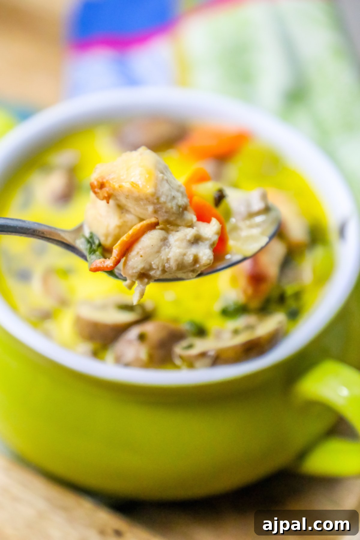 picture of mushroom and chicken soup with thyme on the top in a green pot with a spoonful up close.