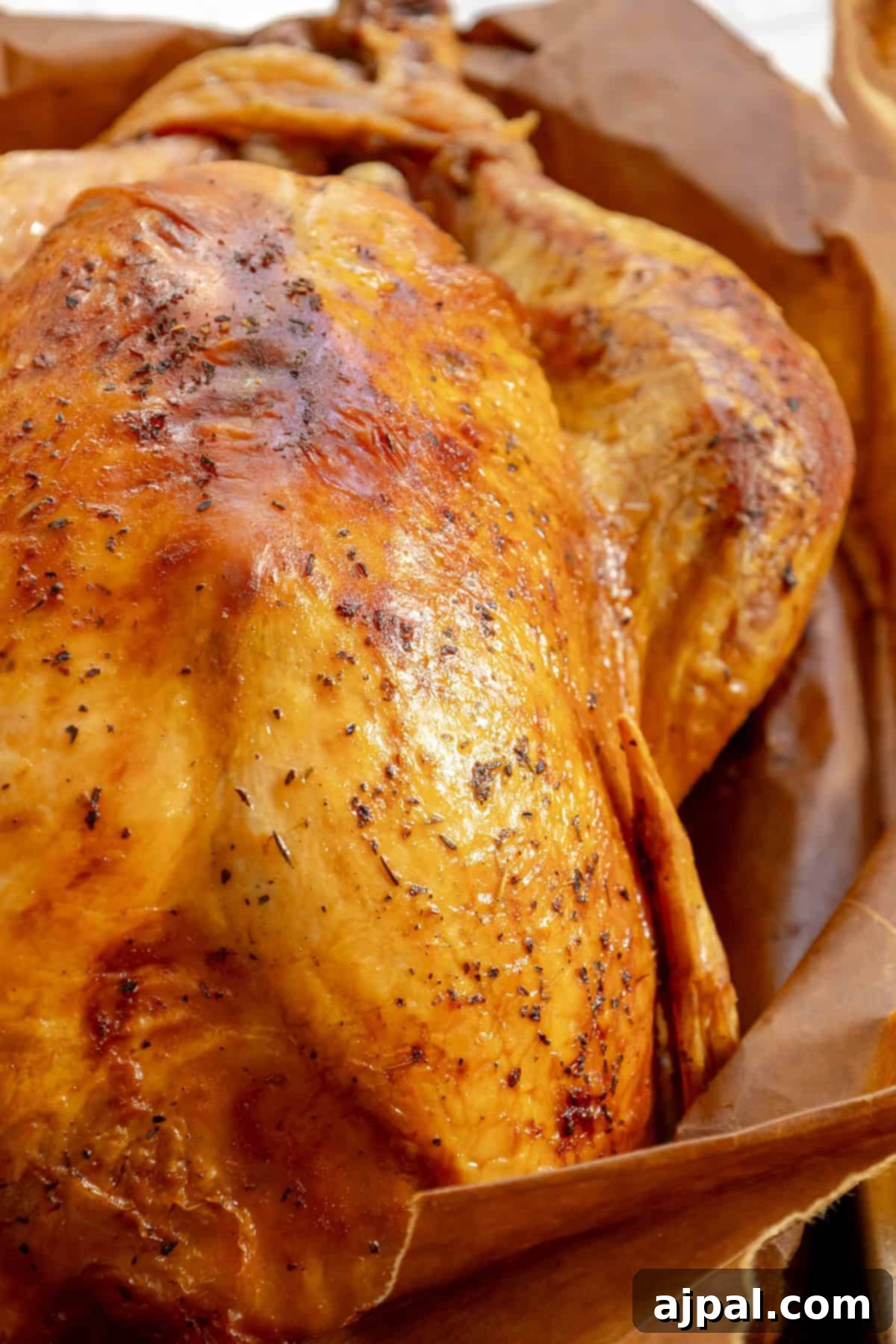 Flavorful Herb Roasted Turkey in a Bag 3 Close-up of a golden-brown roasted chicken resting on parchment paper, reminiscent of the crispy skin and rich seasoning you'd find in the easiest way to cook turkey using a classic brown bag method.
