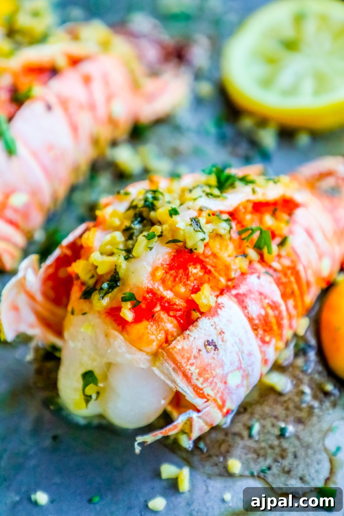 Three garlic broiled lobster tails expertly prepared with lemon wedges and fresh herbs on a rustic wooden baking sheet.