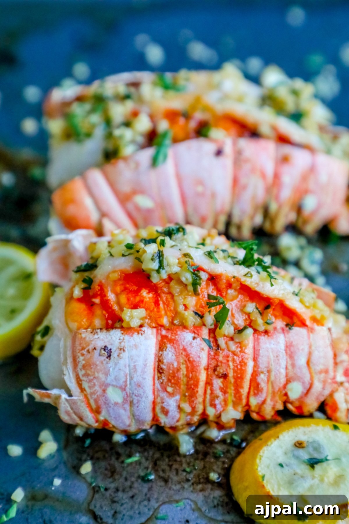 Two perfectly cooked garlic broiled lobster tails presented with fresh lemon wedges on a baking sheet, garnished with herbs.