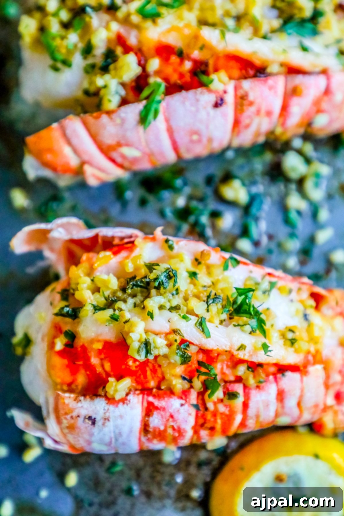 A close-up of two sizzling lemon garlic butter broiled lobster tails, garnished with fresh parsley, served on a baking sheet with extra lemon wedges.