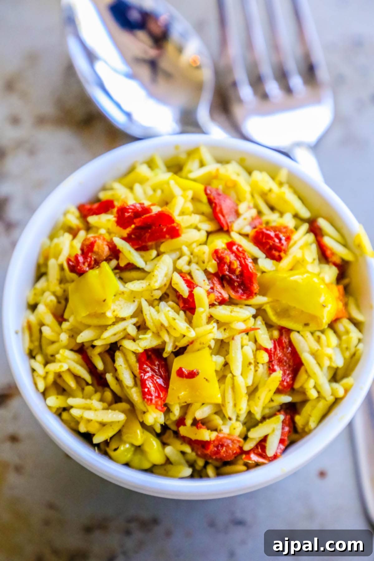 Sun-Dried Tomato and Basil Pesto Orzo 4 A rustic bowl of orzo pasta salad, elegantly garnished with fresh basil, sun-dried tomatoes, and vibrant peppers, creating an inviting presentation.