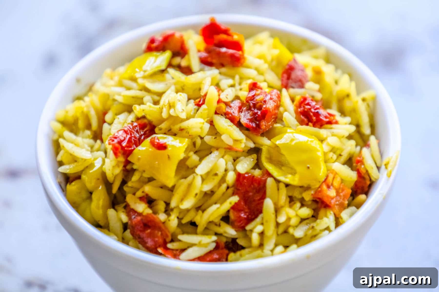 Sun-Dried Tomato and Basil Pesto Orzo 5 A vibrant bowl of orzo pasta salad, elegantly garnished with fresh basil, sun-dried tomatoes, and vibrant peppers, creating an inviting presentation.