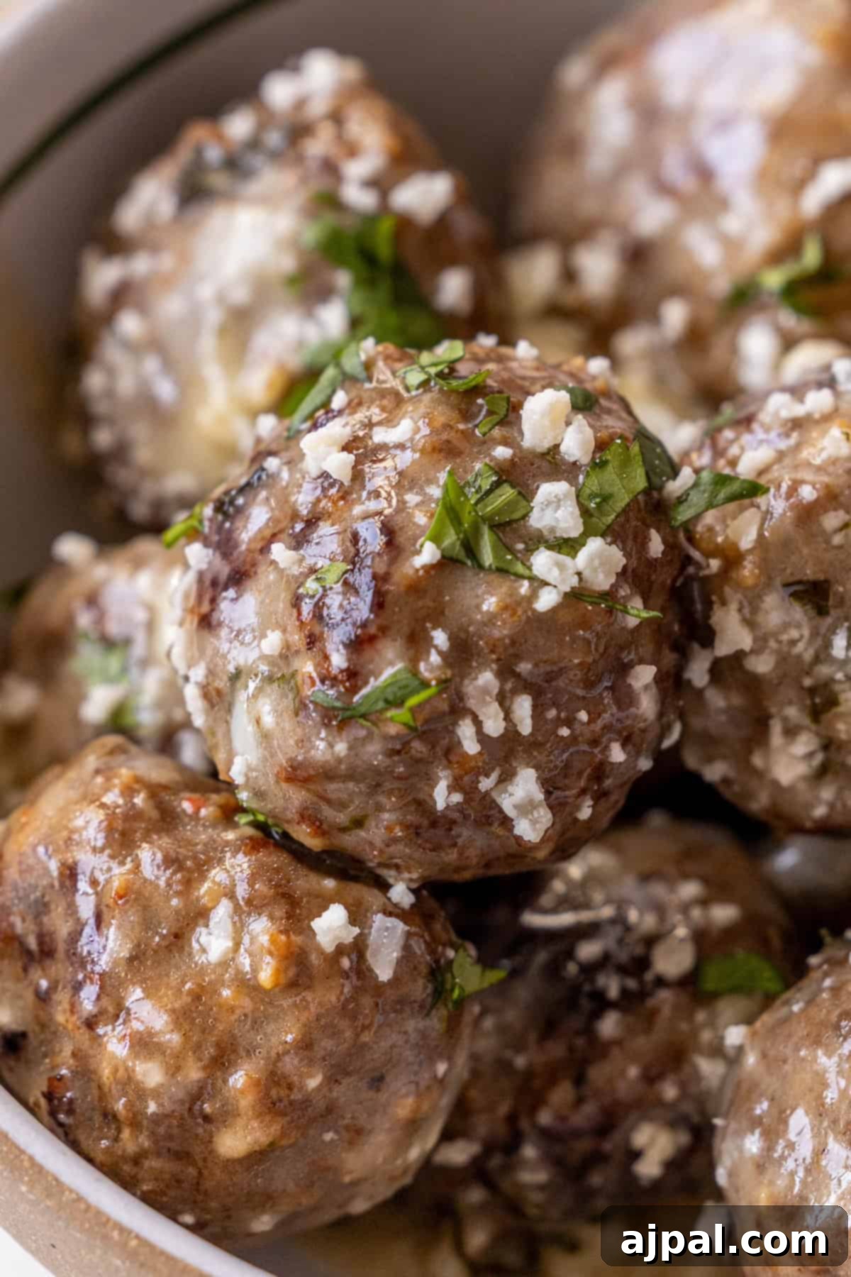 Close-up of a bowl of Garlic Butter Parmesan Meatballs, topped with chopped herbs and grated cheese, ready to be served.