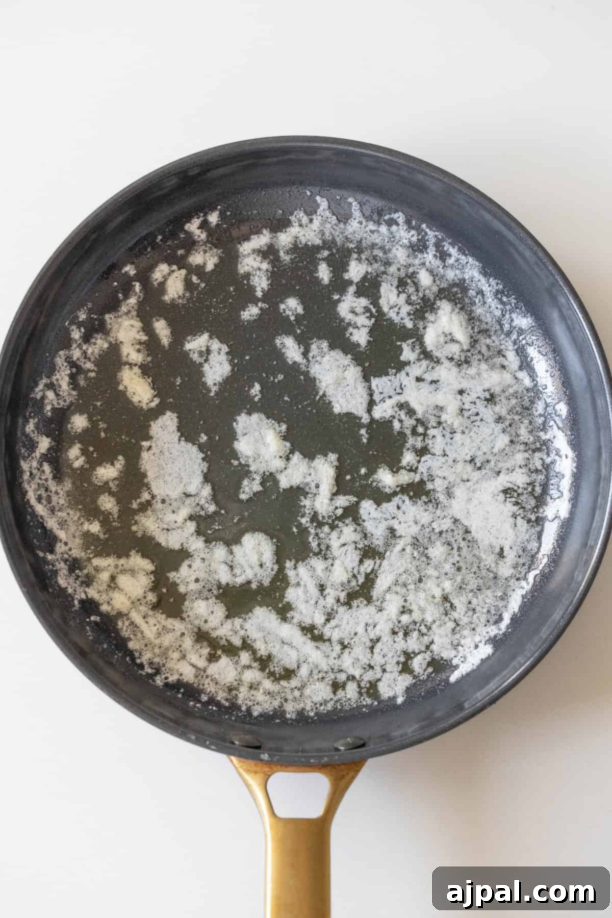 A frying pan with melted butter spread across the surface, ready for cooking Garlic Butter Parmesan Meatballs.