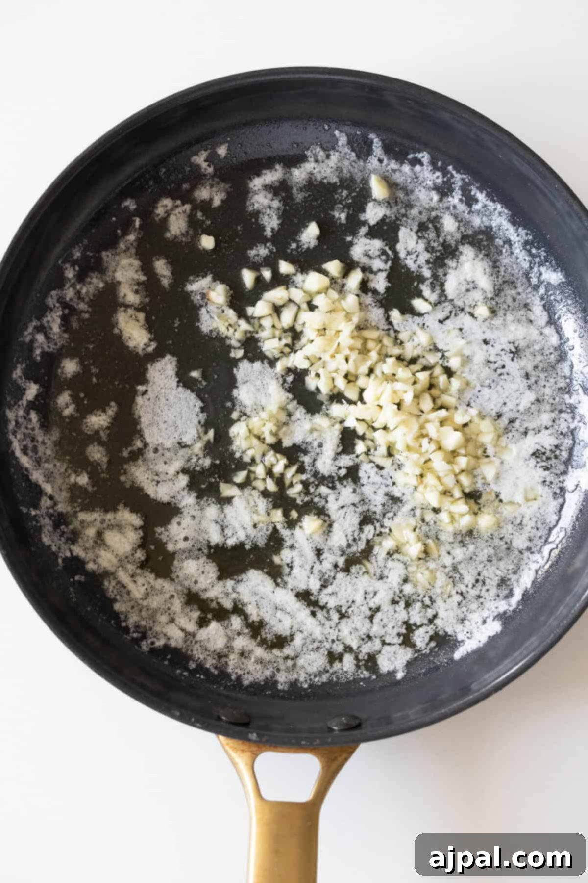 A frying pan with melted butter and chopped garlic on a white background, the beginning of a delicious one-pot dinner.