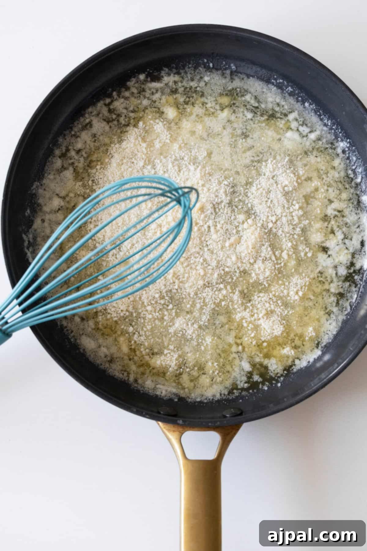 A whisk stirs flour into melted butter in a black saucepan, creating a perfect base for the creamy garlic butter sauce.