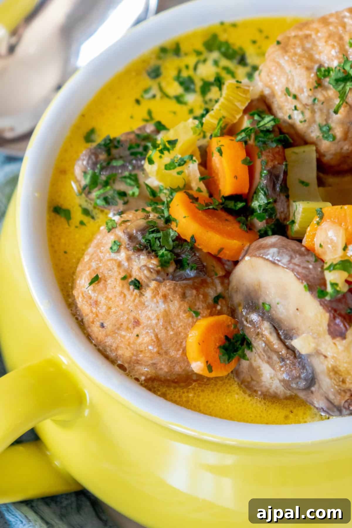 Rich & Creamy One-Pot Meatball Delight 11 A vibrant yellow keto meatball soup with sliced mushrooms, carrots, and sprinkled herbs, served in a matching yellow bowl. Enjoy this easy meatball recipe that’s perfect for those wanting a delicious one-pot meal.