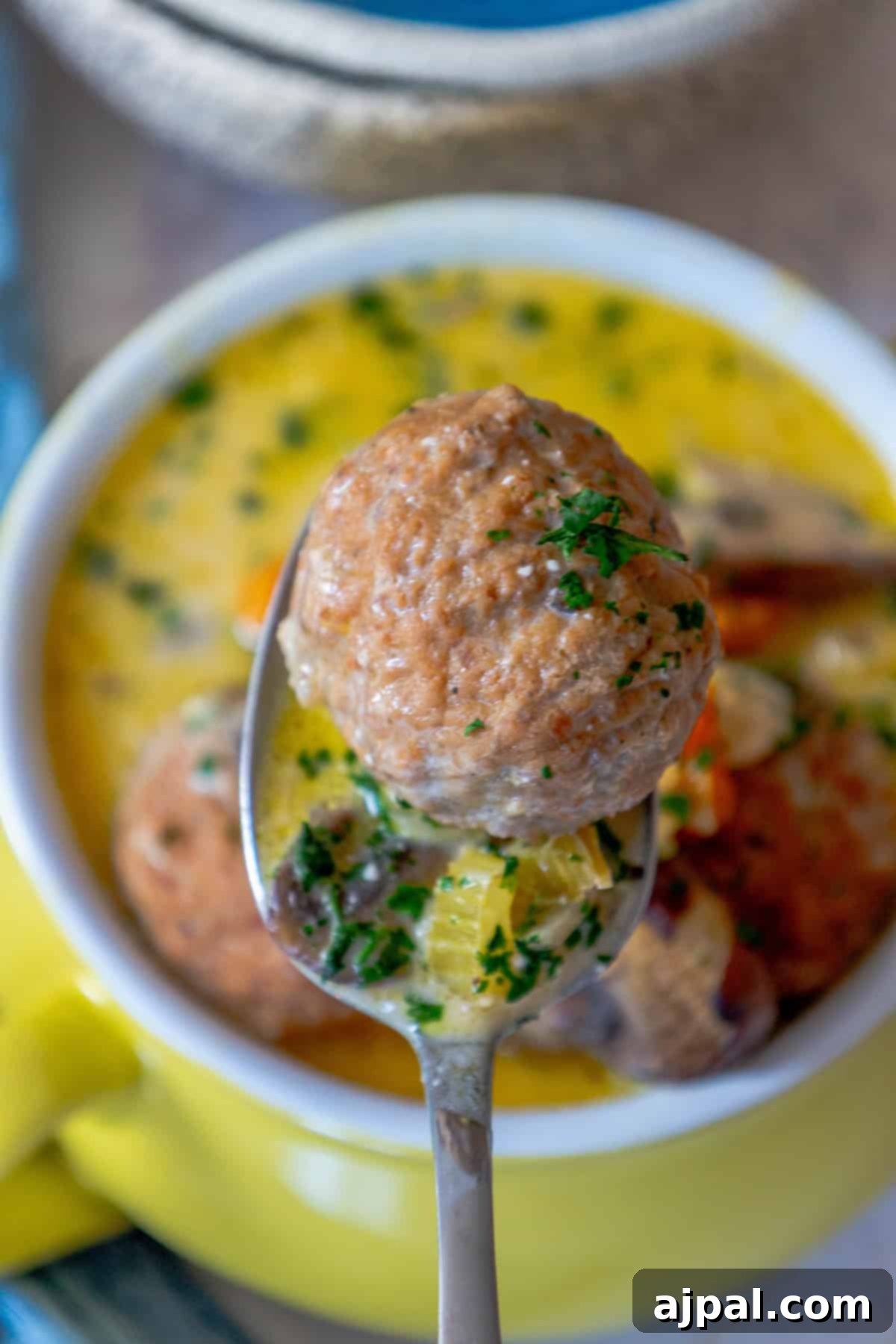 Rich & Creamy One-Pot Meatball Delight 12 A spoon holds a savory meatball with herbs above a bowl of one-pot creamy meatball soup, garnished with fresh parsley.
