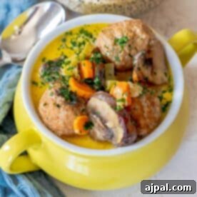 A delicious yellow bowl of keto meatball soup features tender meatballs, carrots, mushrooms, and herbs. A silver spoon rests beside the bowl on a blue cloth, inviting you to savor this comforting one pot meal.