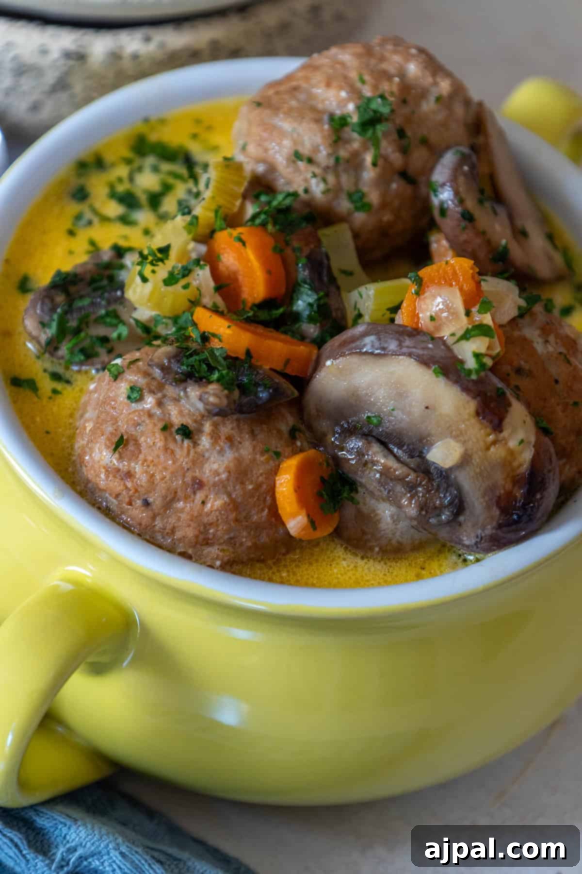 Rich & Creamy One-Pot Meatball Delight 4 Close-up of a yellow bowl with keto meatball soup, featuring savory mushrooms, carrots, and herbs in a creamy sauce.