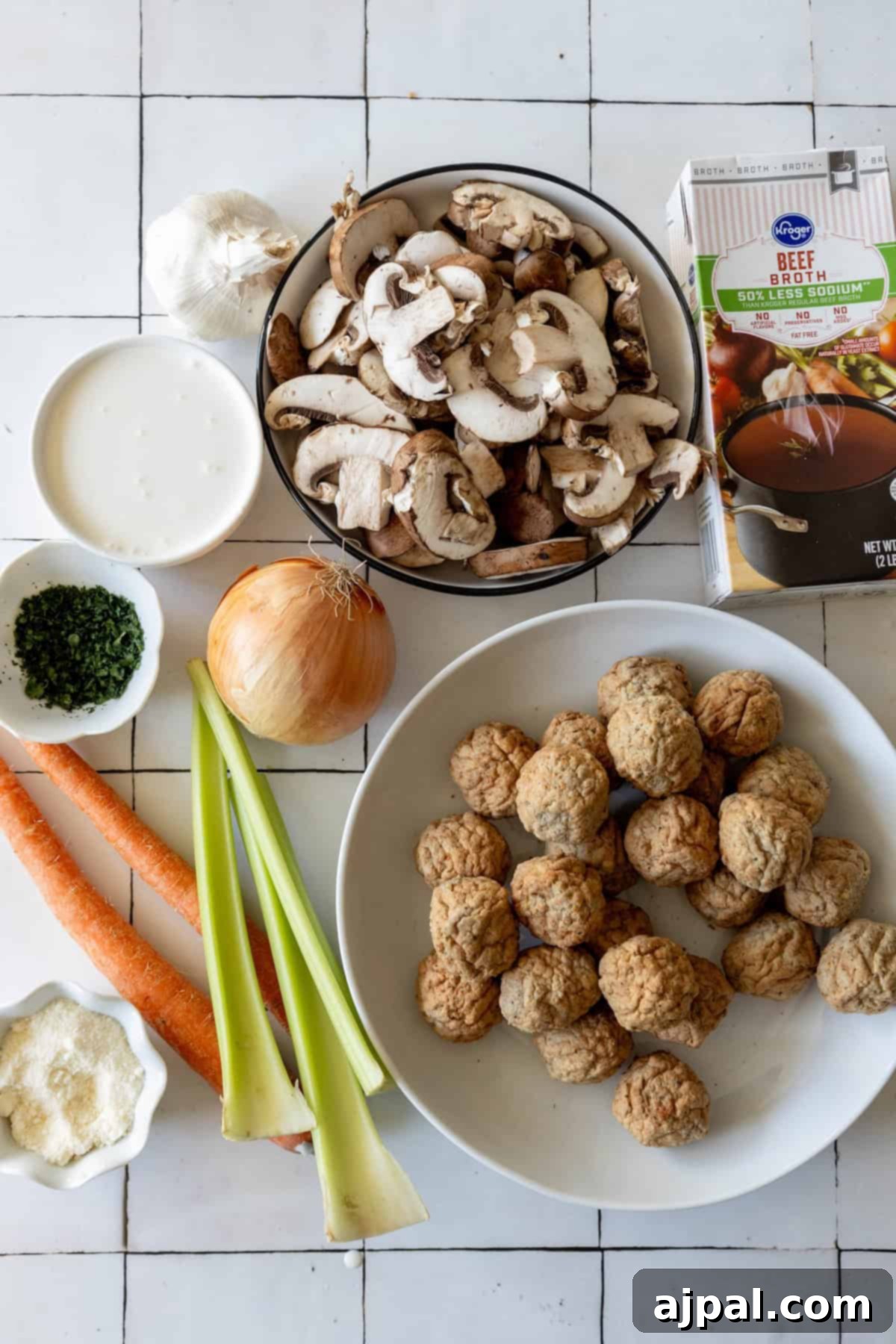 Rich & Creamy One-Pot Meatball Delight 5 A delightful array of ingredients lies before you on the tiled surface, perfect for crafting a delicious one pot meatball soup recipe: mushrooms, a broth carton, garlic, cream, parsley, onion, carrots, celery, grated cheese, and savory meatballs.