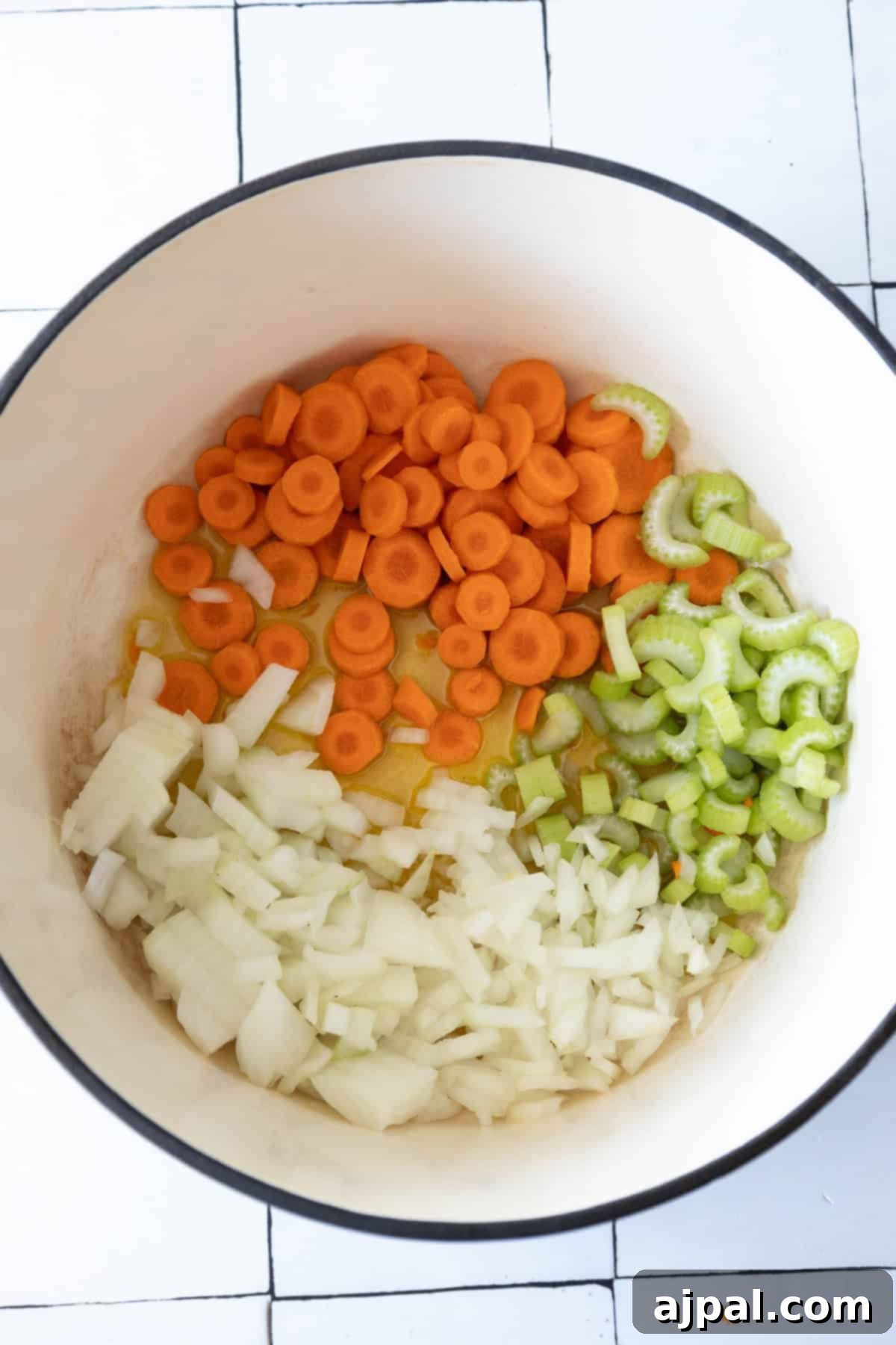 Rich & Creamy One-Pot Meatball Delight 6 Chopped carrots, celery, and onions in a large white pot on a tiled surface set the stage for a comforting one pot meatball soup recipe.