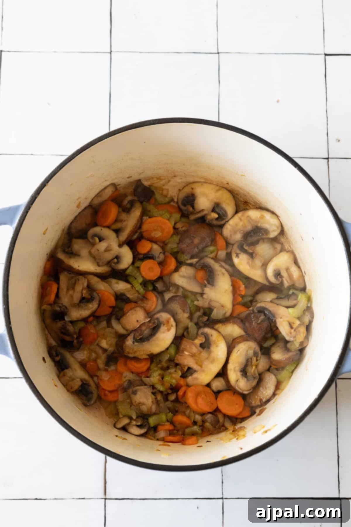 Rich & Creamy One-Pot Meatball Delight 7 A pot filled with sliced mushrooms, carrots, and other vegetables sits on a tiled kitchen floor, ready to transform into a delicious one-pot creamy meatball soup.