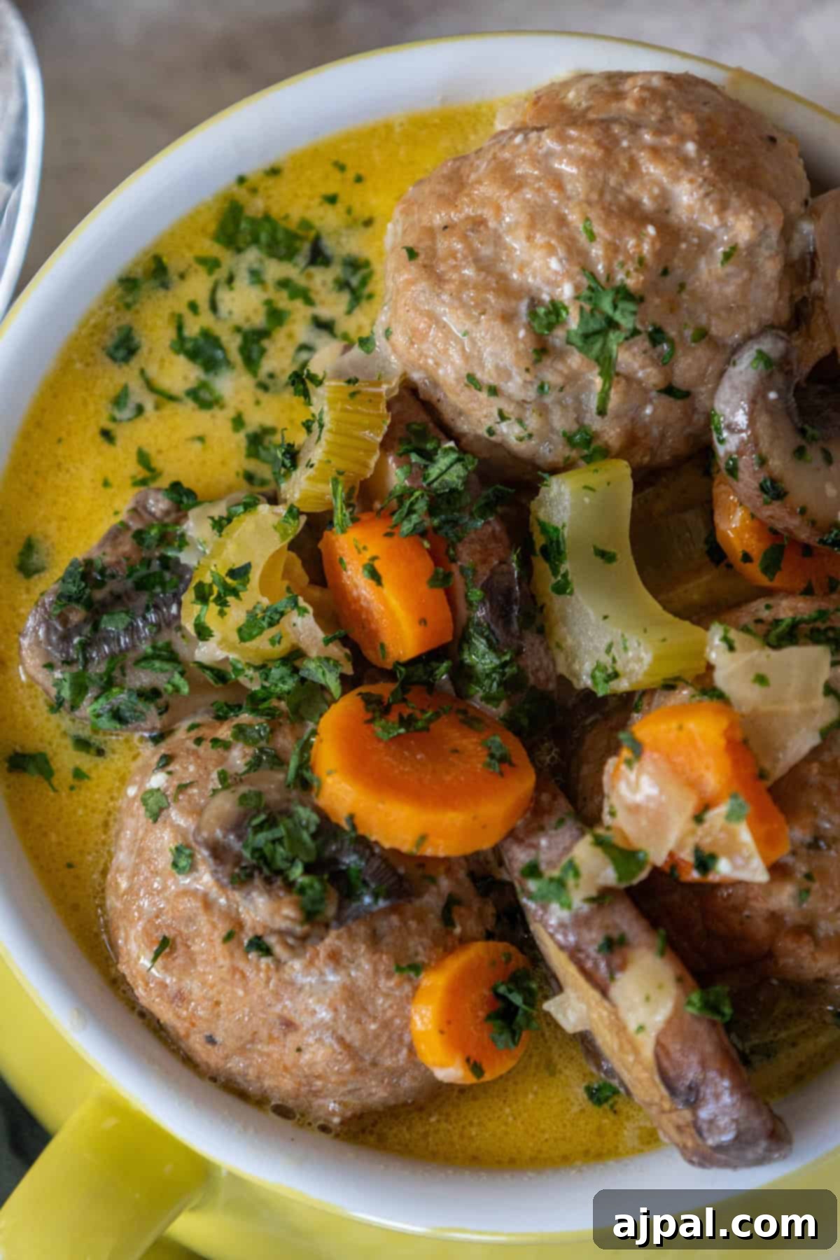 Rich & Creamy One-Pot Meatball Delight 10 A delightful bowl of meatball soup featuring a keto-friendly mix of sliced carrots, celery, mushrooms, and herbs in a luscious yellow broth. This one-pot creamy meatball soup is both hearty and satisfying for any meal.