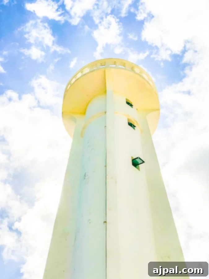 A striking white lighthouse stands tall against a clear blue sky, overlooking the serene blue waters of a tropical bay.