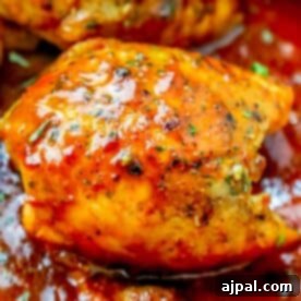 Sizzling Skillet BBQ Chicken Thighs 10 A close-up of golden-brown chicken thighs glazed with spicy, herb-infused sauce in a skillet. This keto chicken thigh skillet dinner features visible herbs and a glossy finish, nestled in thick red sauce for an irresistible touch.