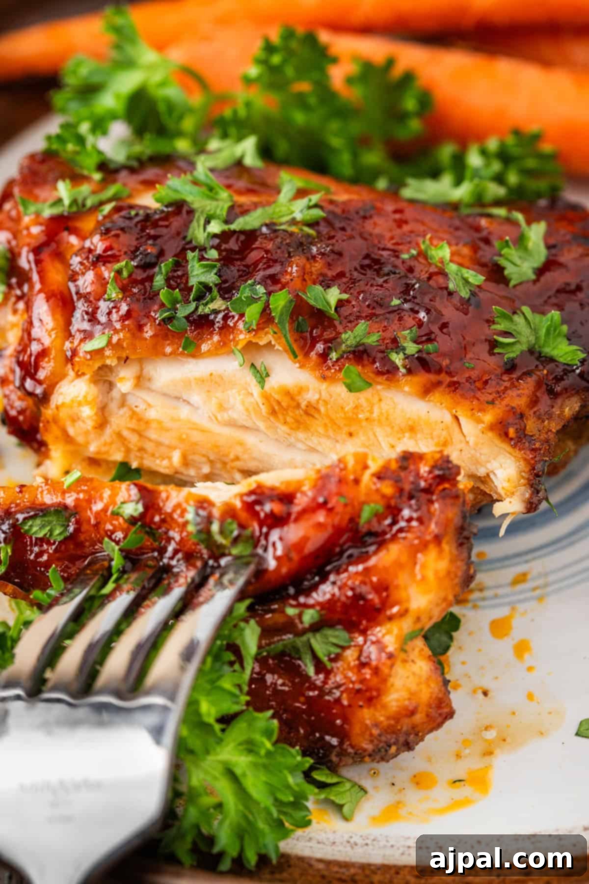 Sizzling Skillet BBQ Chicken Thighs 8 Close-up of a fork slicing into a glazed chicken breast garnished with fresh parsley on a plate, with carrots in the background, capturing the essence of an easy one-pan BBQ chicken thigh skillet dinner.